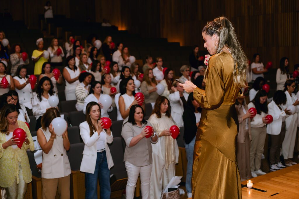 Oradora com microfone diante de uma plateia, durante um evento.