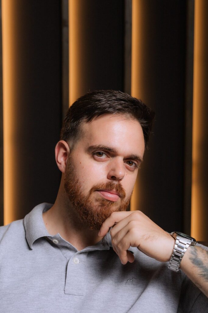 Homem de polo cinzento, mão no queixo, retrato profissional de perto para perfil profissional.