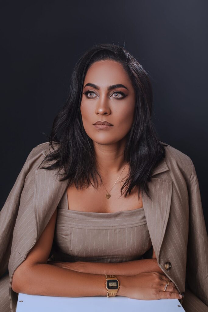 Mulher de fato bege risca de giz, sentada, retrato de marca pessoal em estúdio com fundo escuro.