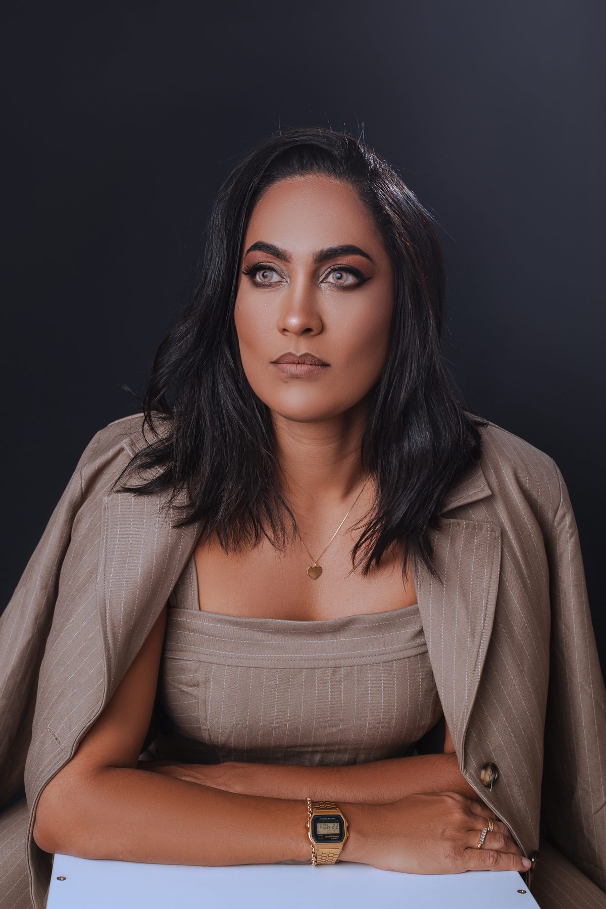 Mulher de fato bege risca de giz, sentada, retrato de marca pessoal em estúdio com fundo escuro.