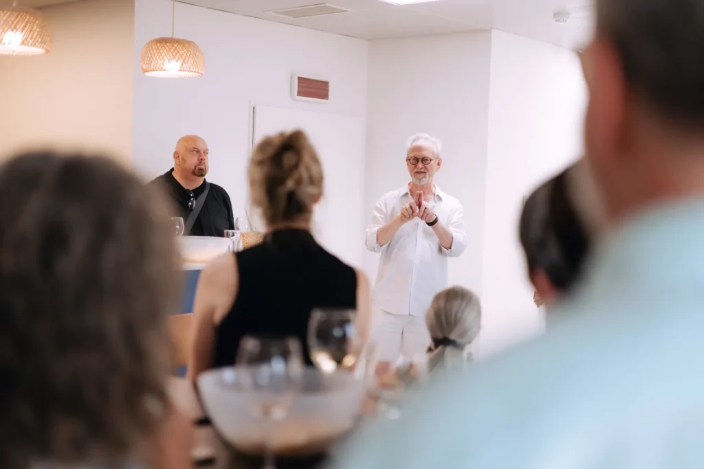 Convidado a discursar de pé durante um almoço de empresa, observado pelos participantes sentados à mesa.