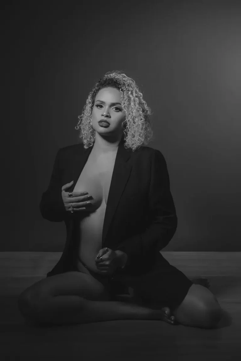 Retrato a preto e branco de uma mulher sentada no chão do estúdio, de blazer preto, a olhar para a câmara.